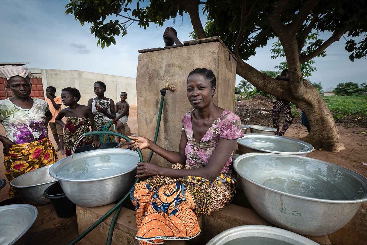 Community water point in Benin: a woman fills basins while others wait with containers.